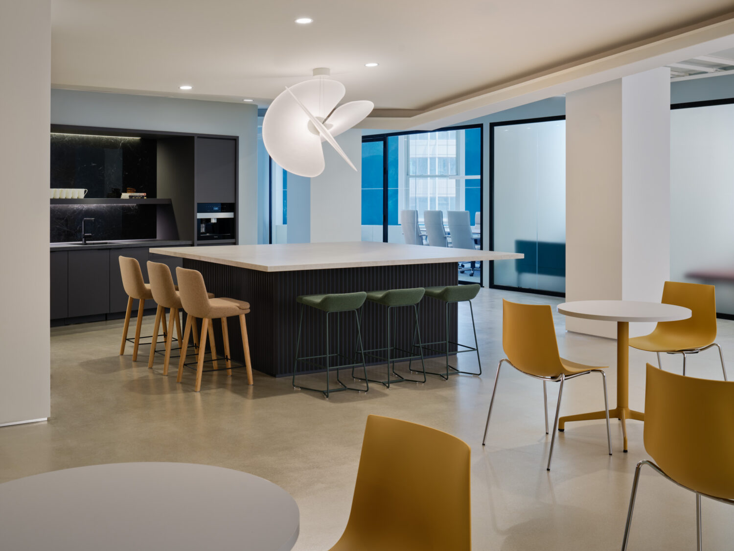 Kitchen island with wood stools and mustard chairs near windows in the Keilhauer showroom