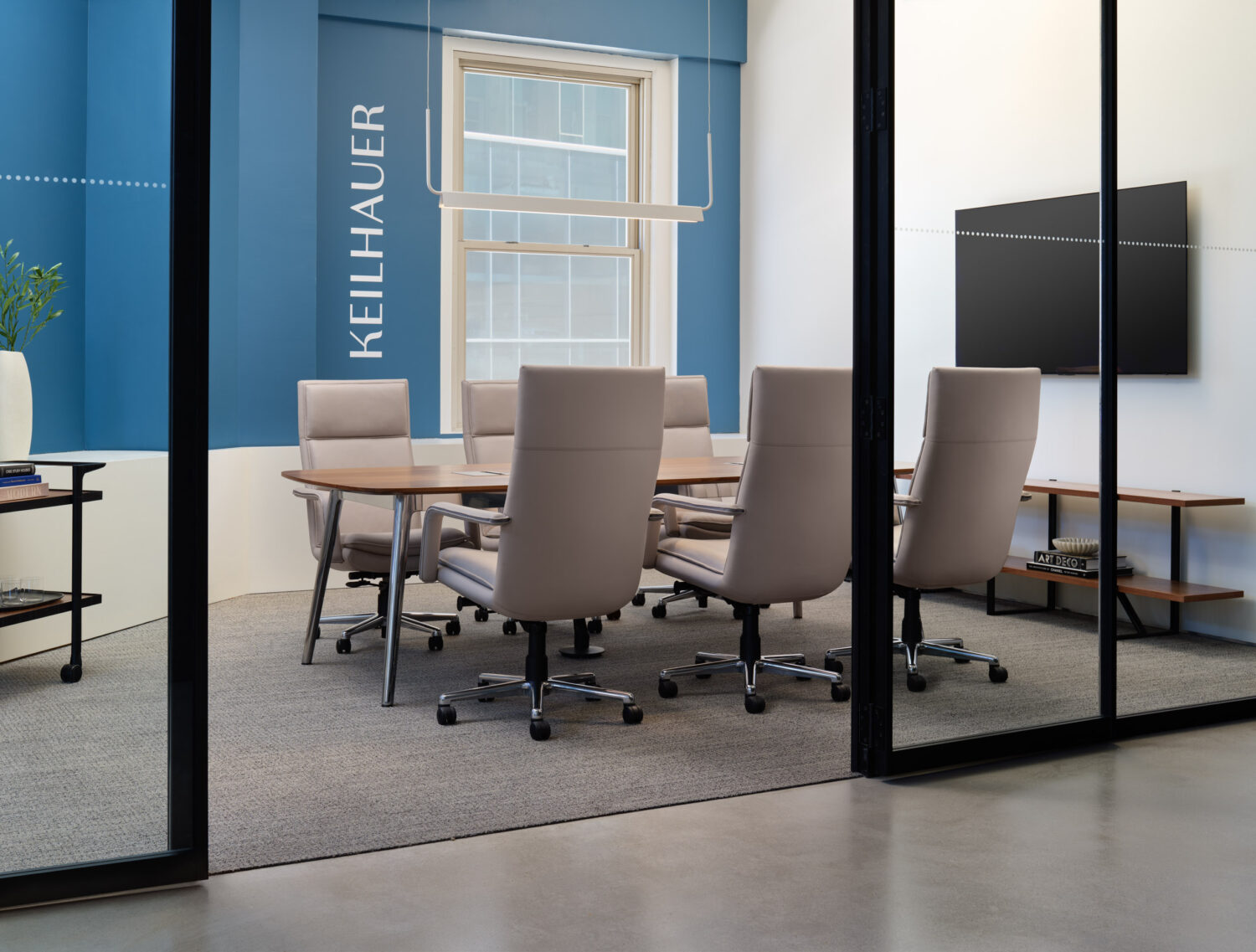 Conference room with a wood table and leather chairs behind blue glass walls in the Keilhauer showroom