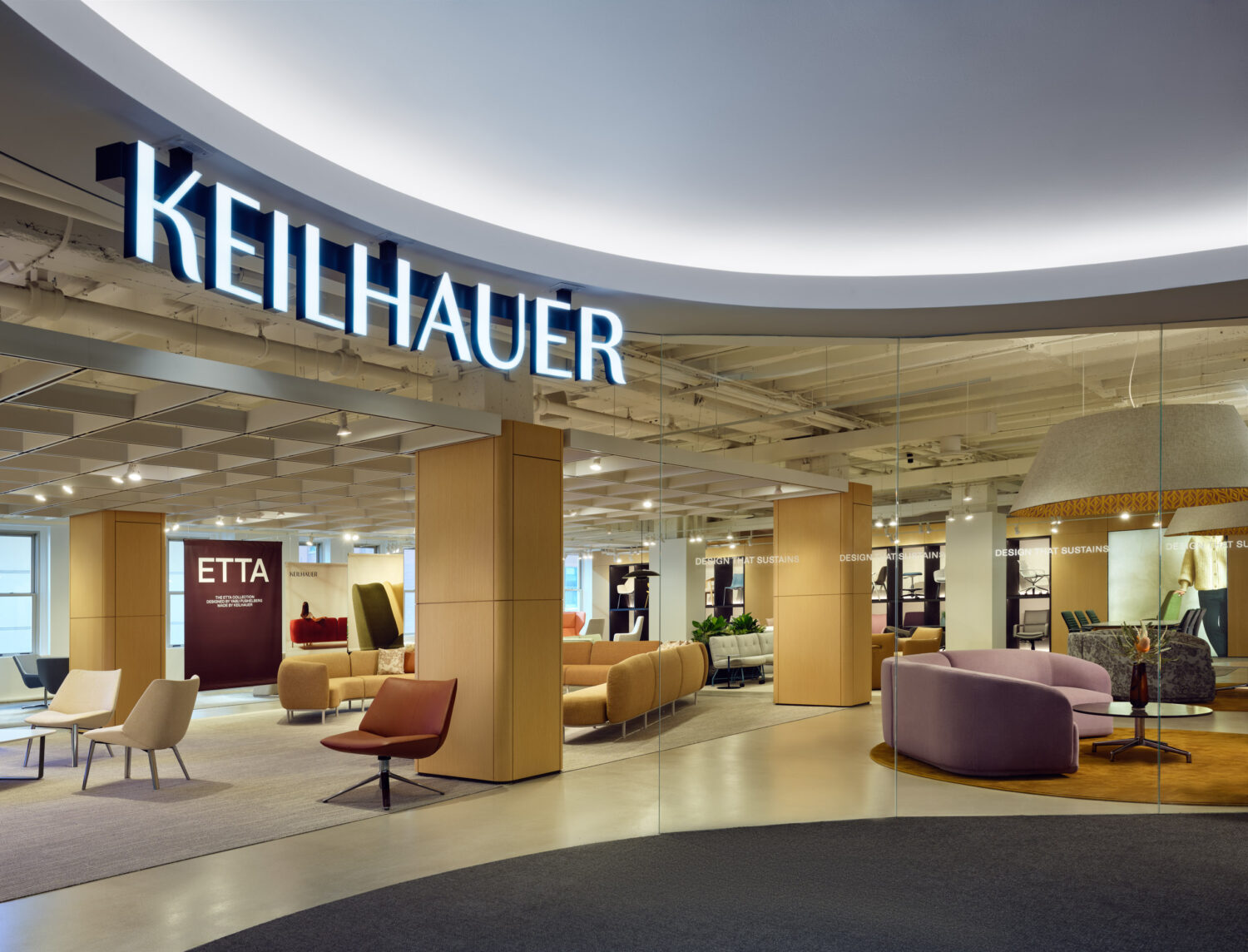 Illuminated Keilhauer sign on a curved ceiling above a warm, busy showroom floor