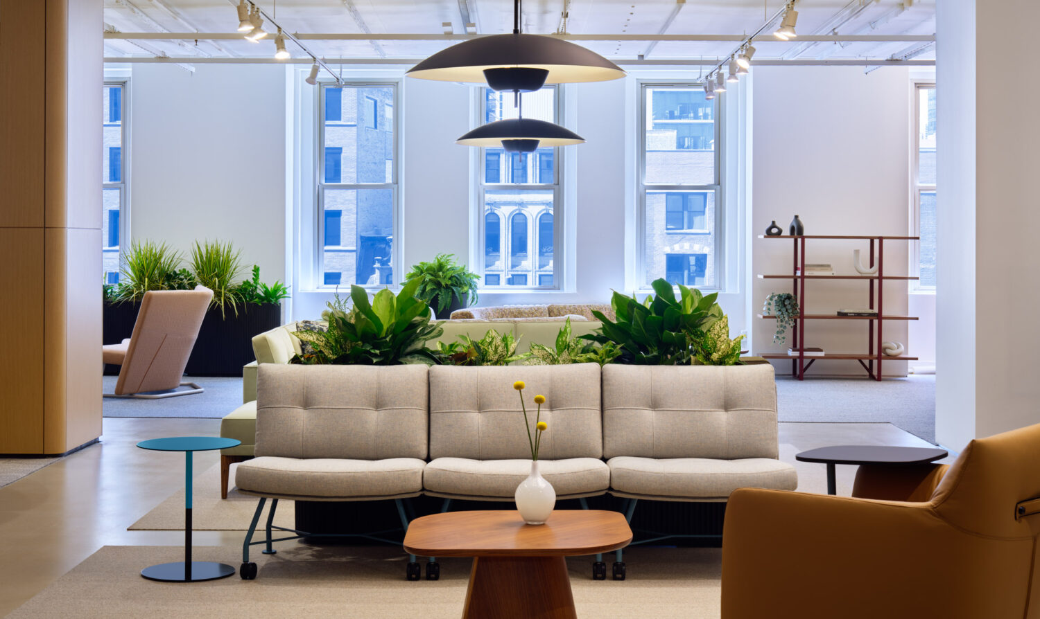 Long cream sofa with planters and pendant lights in front of tall windows in the Keilhauer showroom