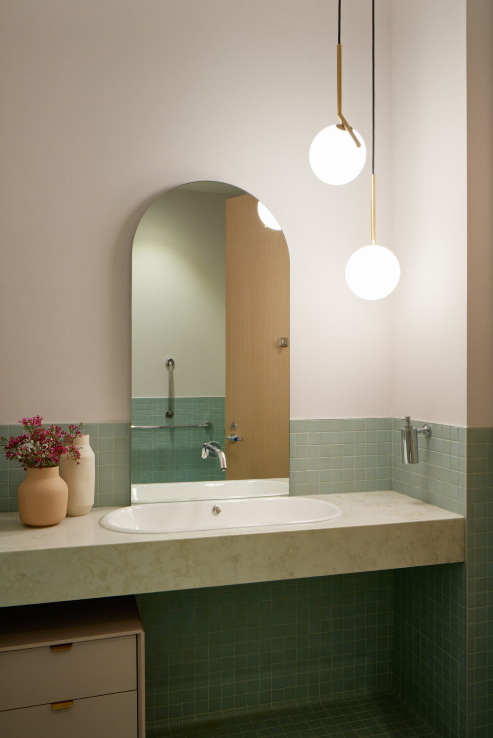 Single restroom with an arched mirror, green tile and brass globe lights at Forward Space