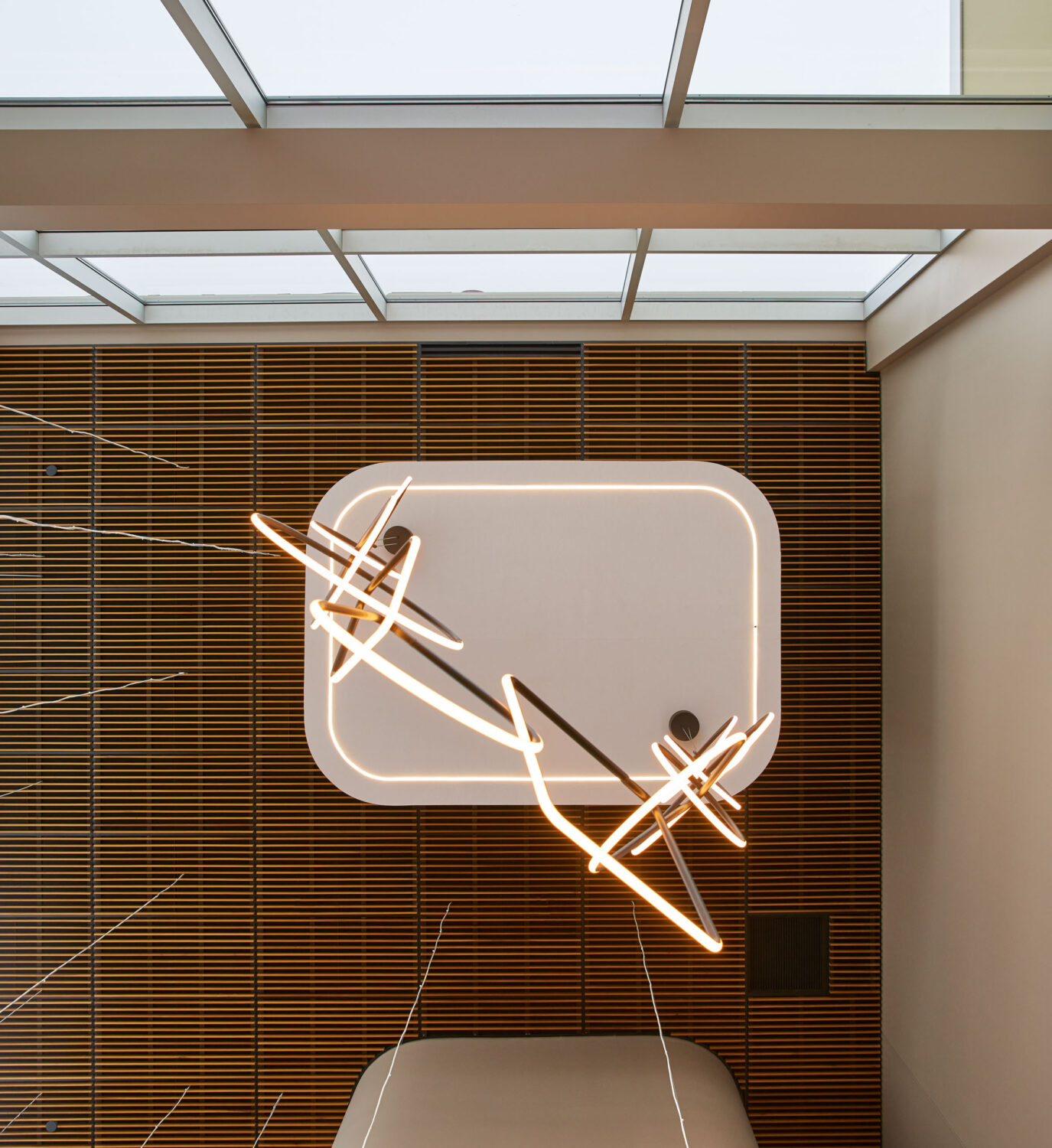 Sculptural light ribbons circling a glowing ceiling frame below a skylight at Forward Space