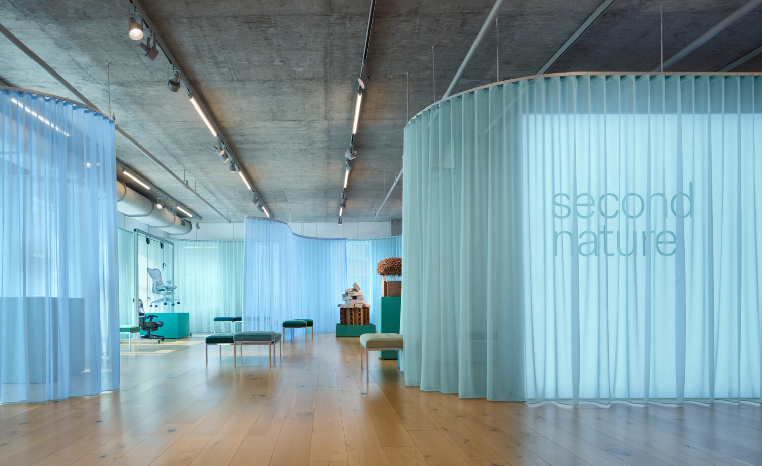 Sheer aqua curtains enclosing a lounge setting under a concrete ceiling in the MillerKnoll showroom