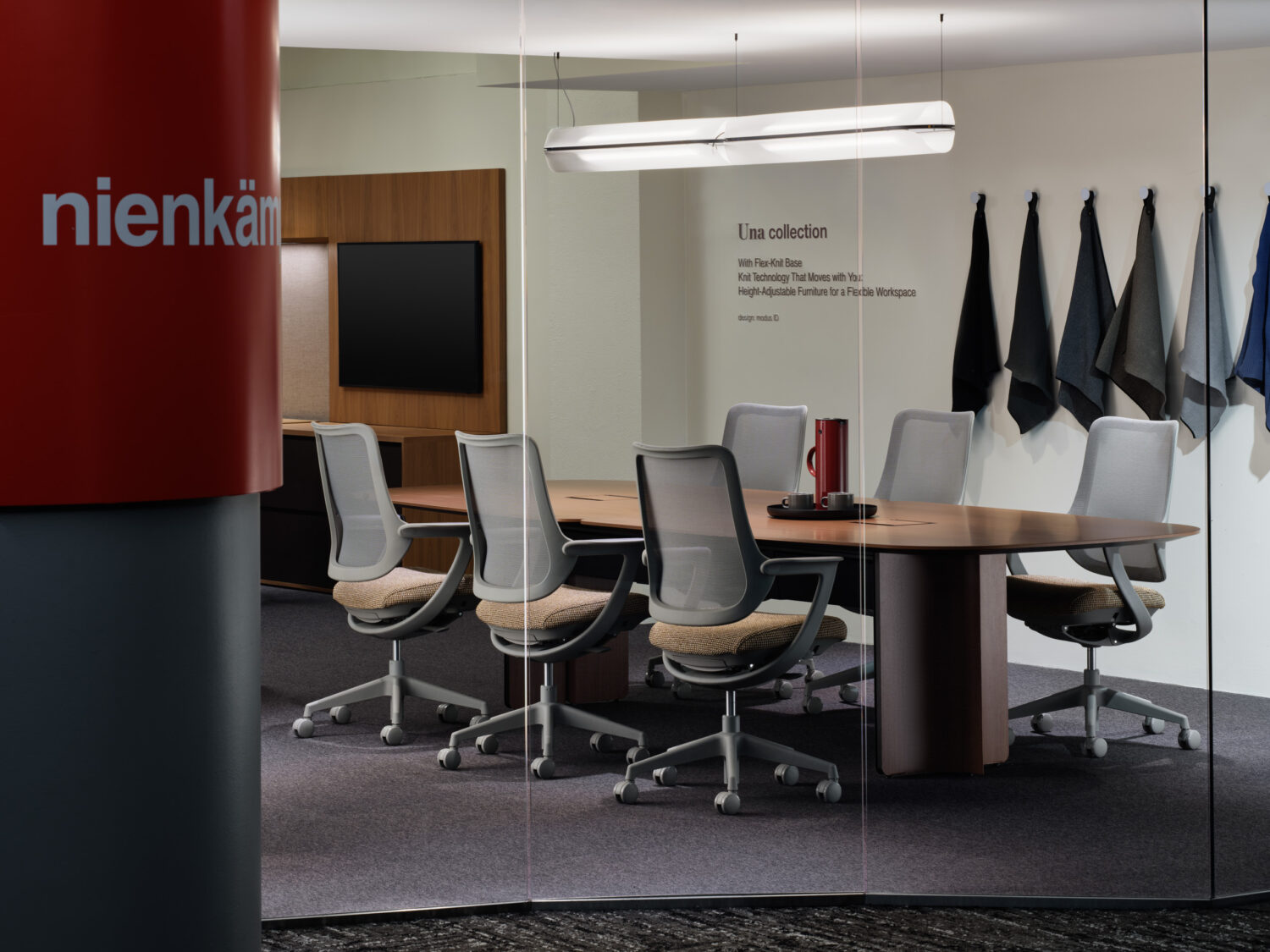 Meeting room with a round wood table and mesh chairs beside a red Nienkämper sign
