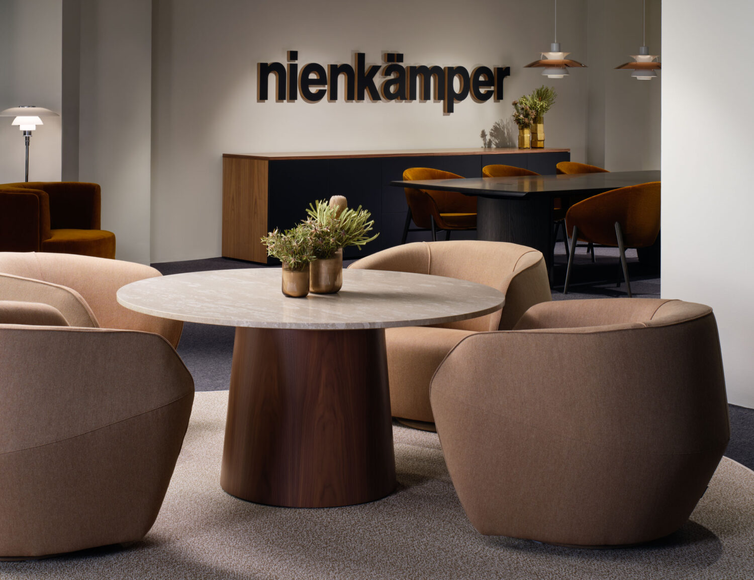 Rounded tan lounge chairs around a wood table beneath the Nienkämper logo