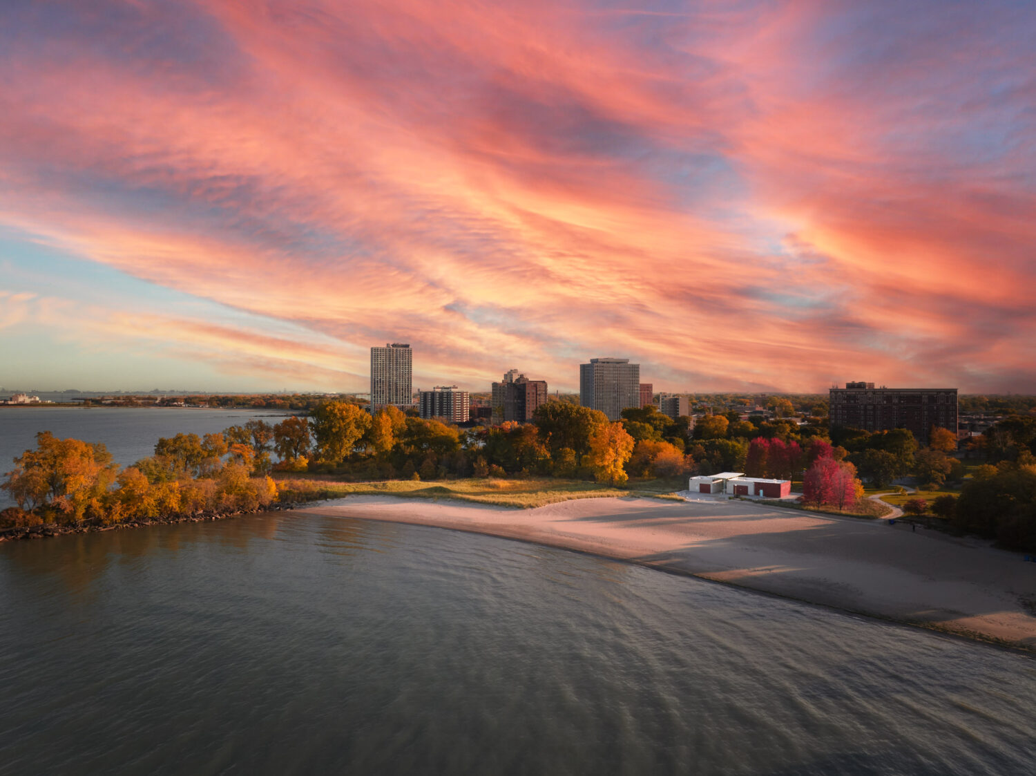 Aerial view of South Shore Beach House on the Lake Michigan shore at sunset, autumn trees and South Shore high-rises under a pink sky