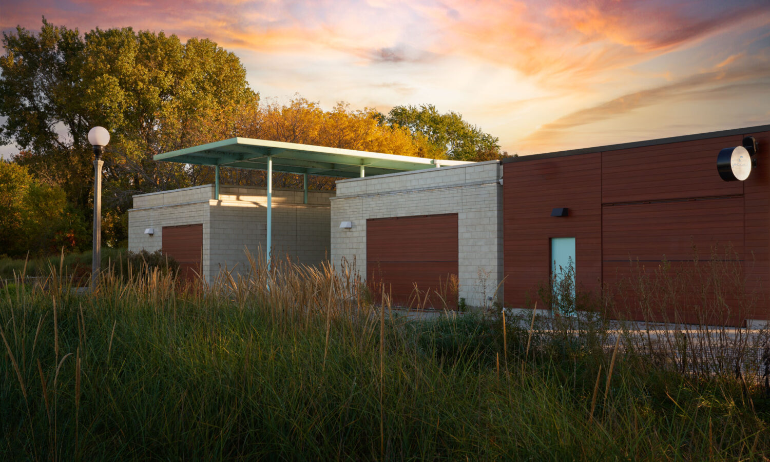Masonry pavilions and pale green floating canopy of South Shore Beach House at sunset behind tall dune grasses