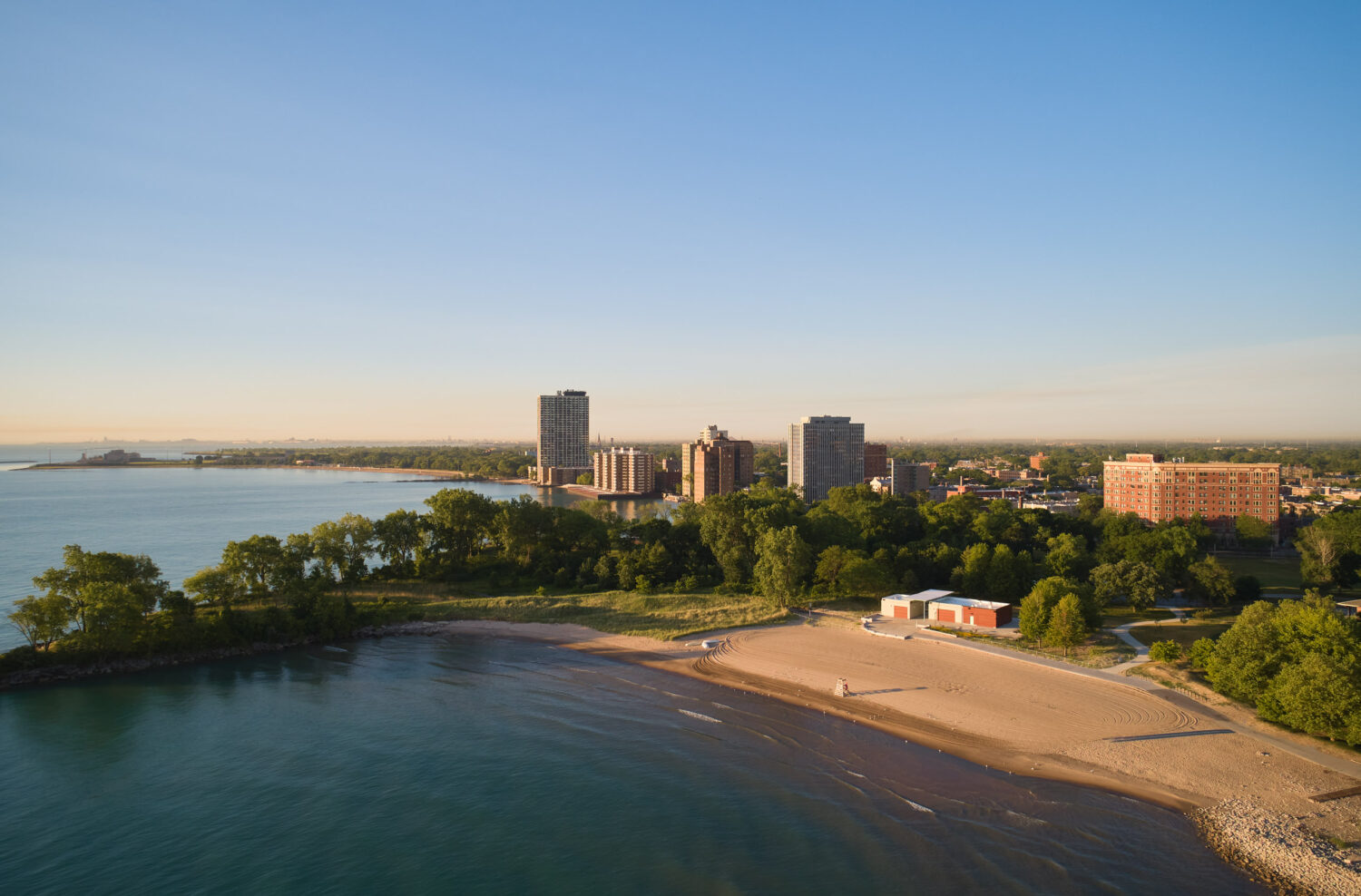 Aerial view of South Shore Beach House on a summer morning, the curving beach and Lake Michigan shoreline with South Shore high-rises beyond