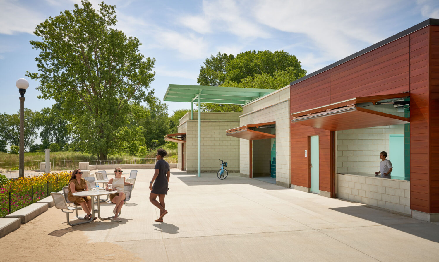 Patio of South Shore Beach House with visitors at tables beneath the green steel canopy and the open concession counter