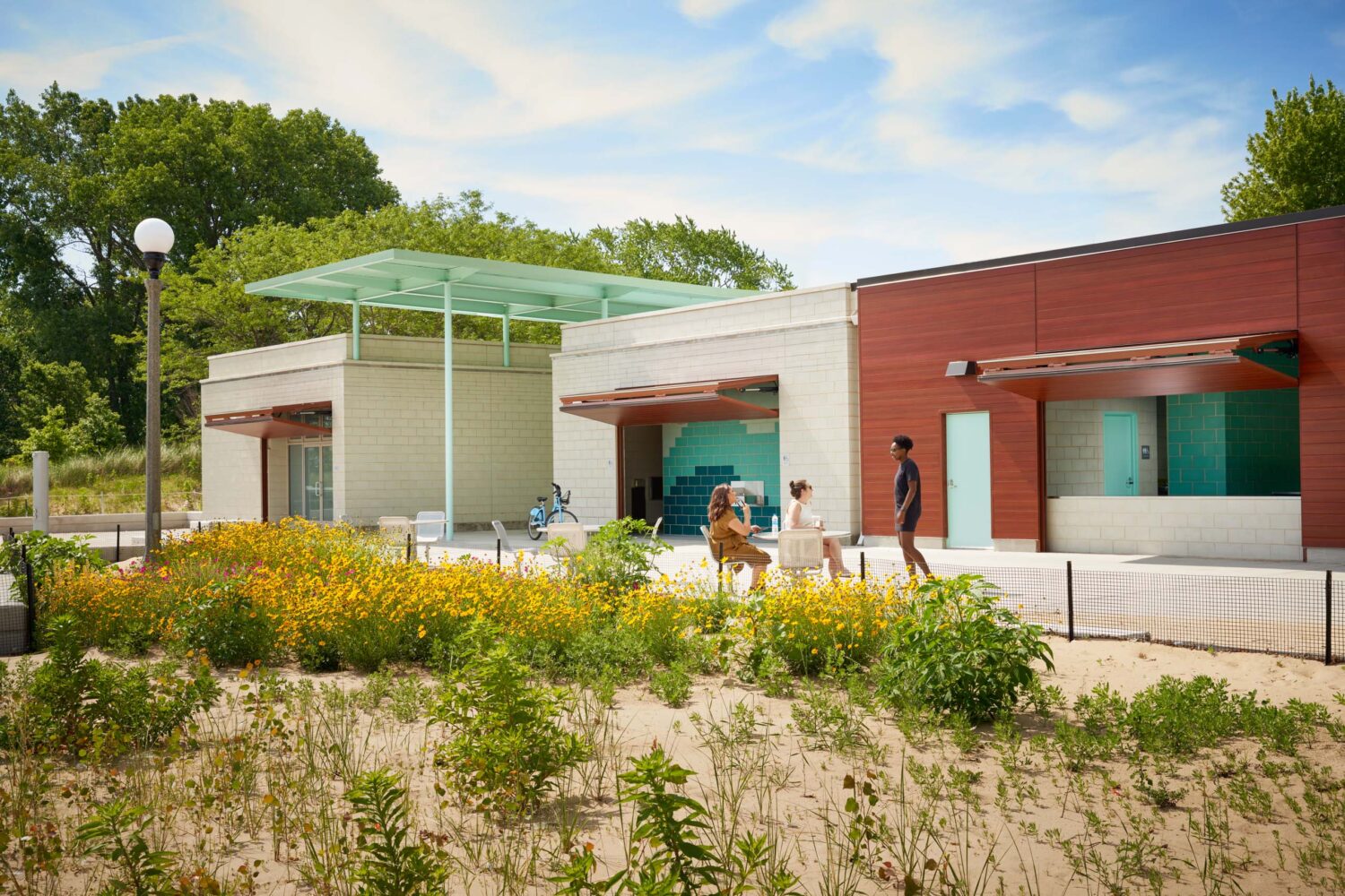 South Shore Beach House pavilions and floating canopy behind yellow wildflowers and dune plantings, visitors on the patio