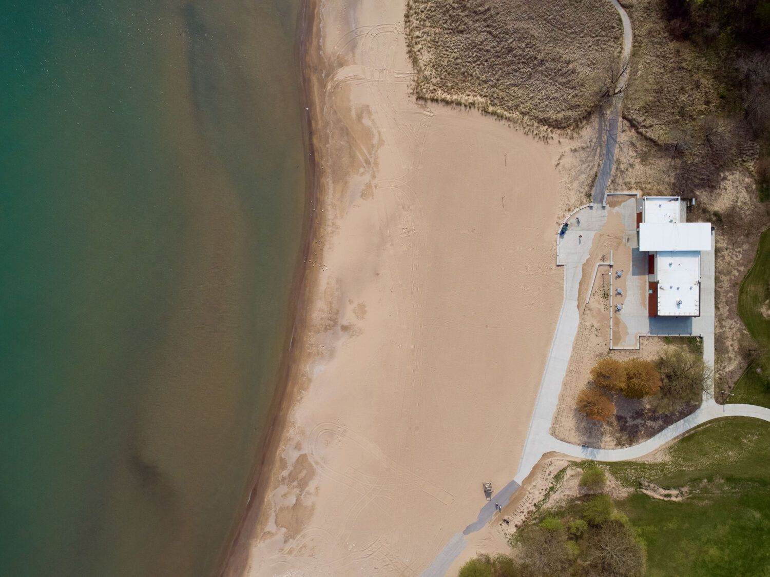 Overhead aerial of South Shore Beach House in summer, the curving beach between Lake Michigan and green dune plantings