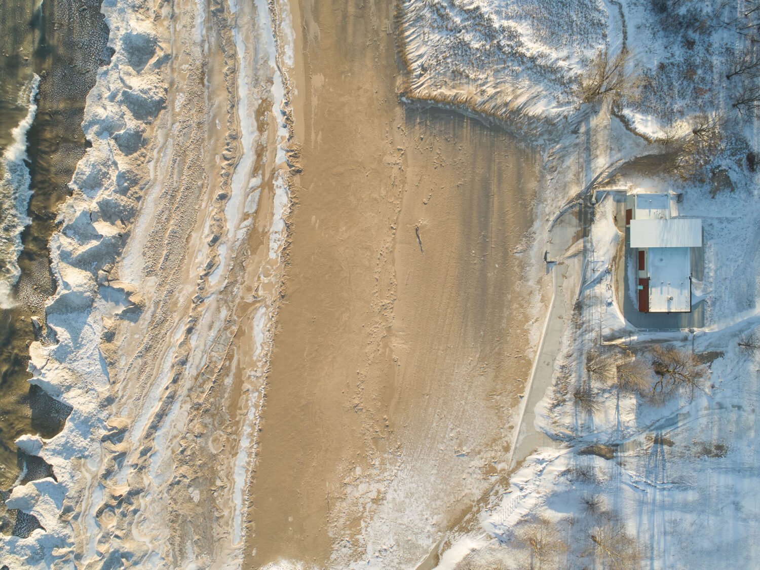 Overhead aerial of South Shore Beach House in winter, ice ridges along the Lake Michigan shore and snow around the building