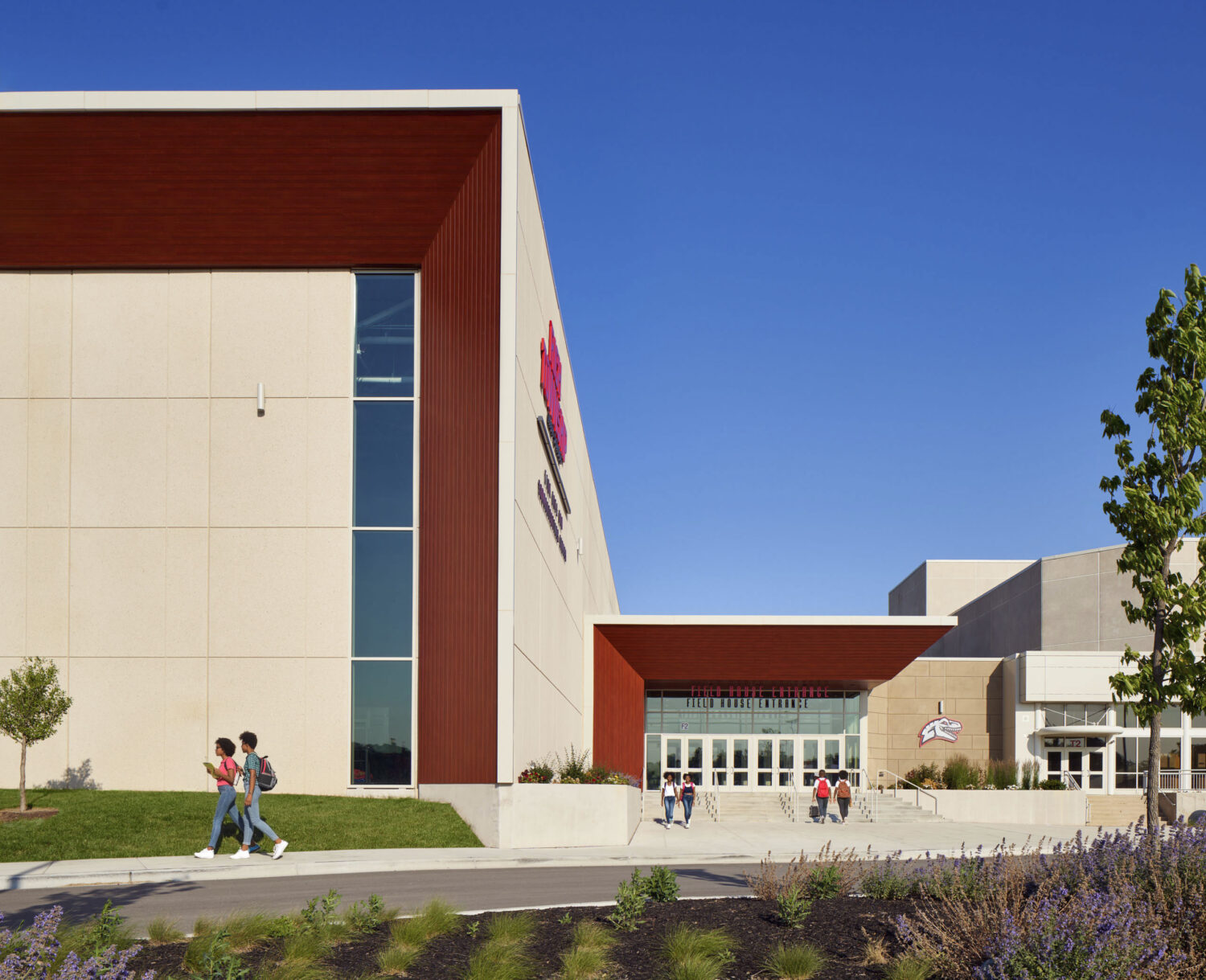 Tall white and red volume framing the glass entrance, with students walking past landscaped beds at Rich Township High School