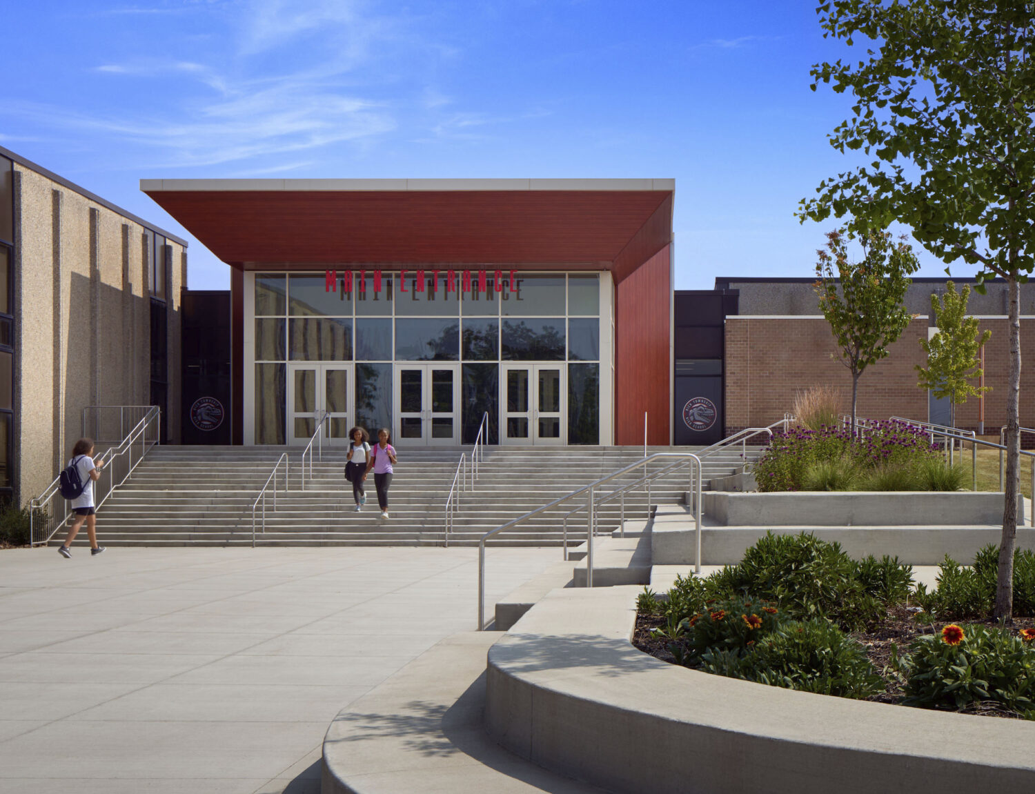 Students climbing broad entry steps to the glass front doors beneath a red canopy at Rich Township High School