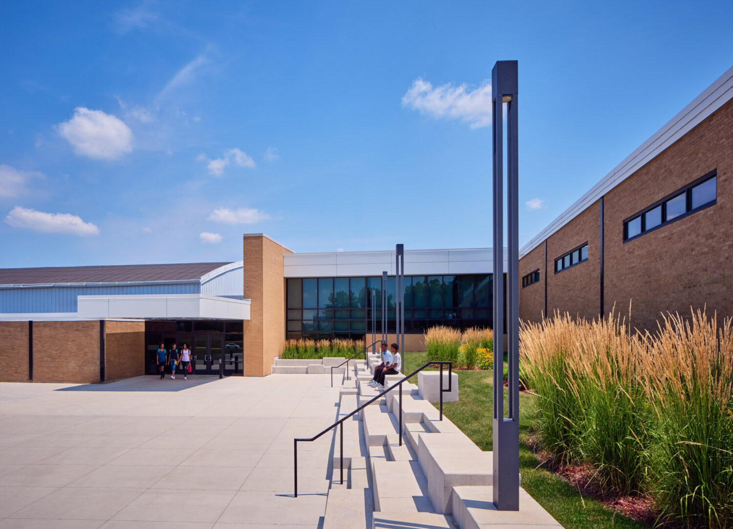 Entry walk with a tall light pole, tiered steps and ornamental grasses beside the brick wing at Rich Township High School