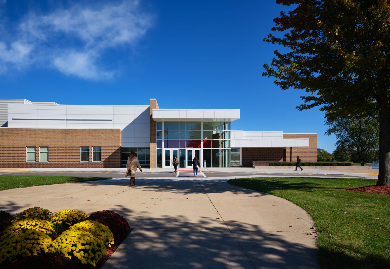 Glass entry pavilion beyond a curved walk and flowering shrubs at Rich Township High School