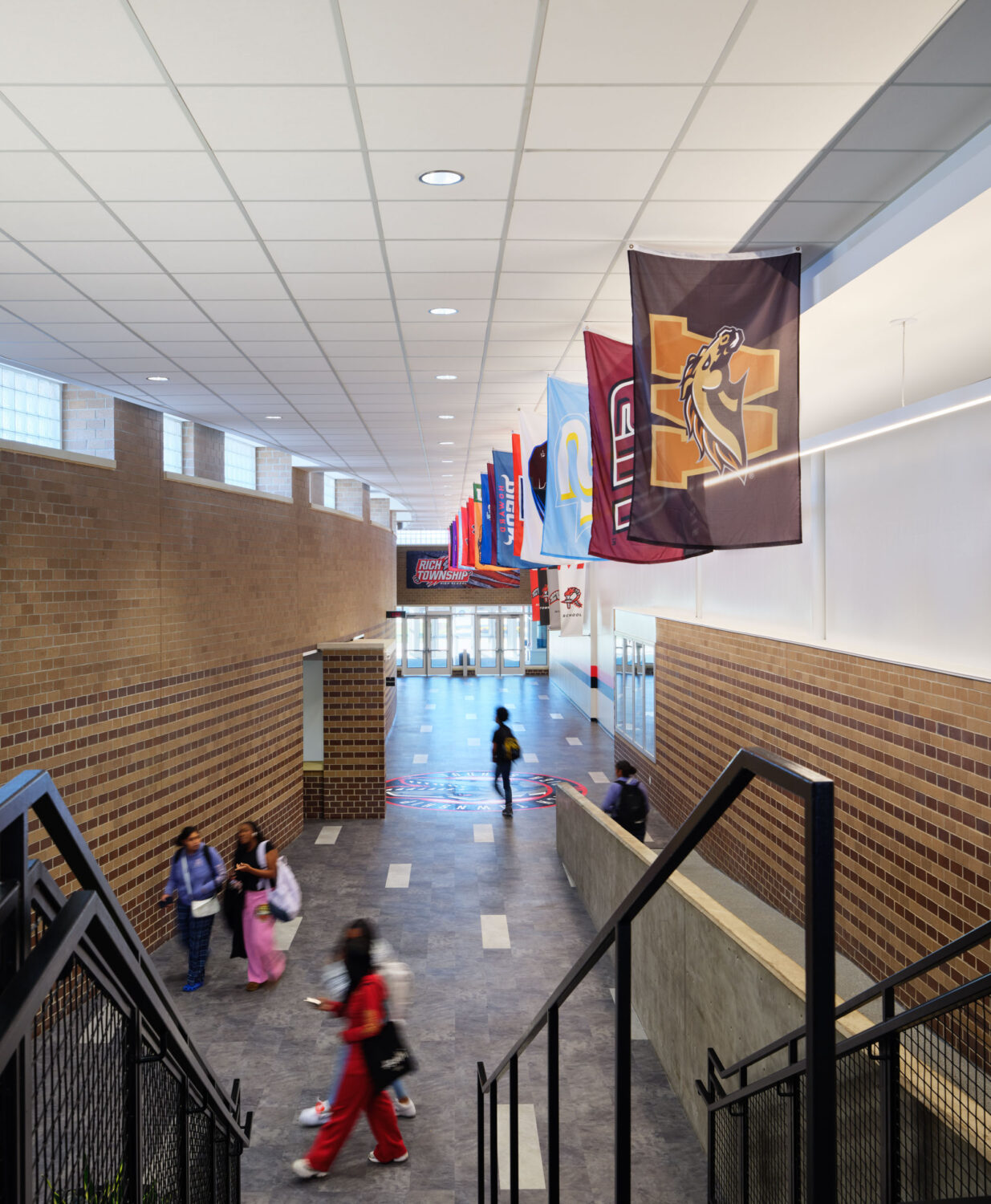 Students walking along an upper-level corridor with hanging banners and a stair at Rich Township High School
