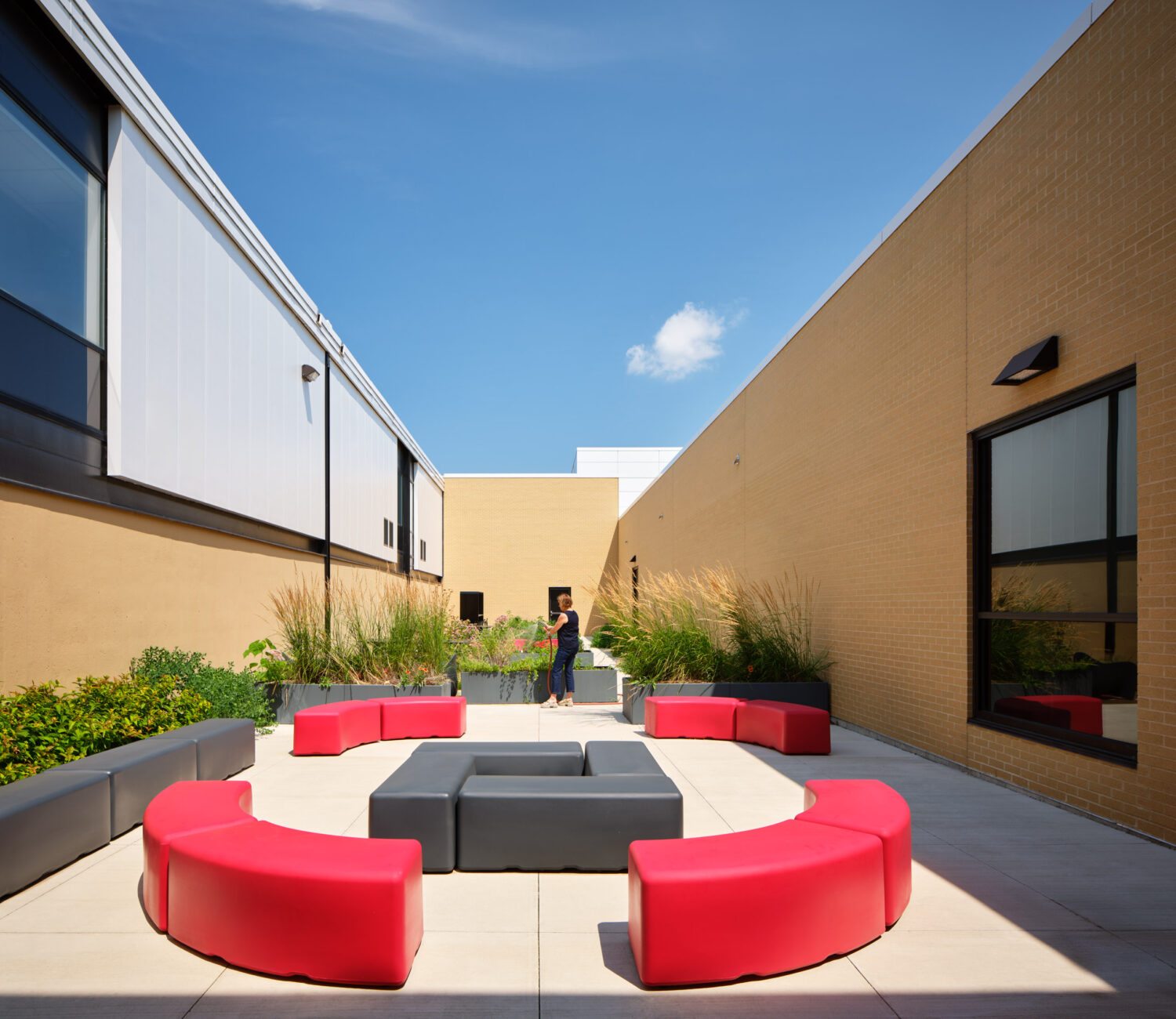 Courtyard with curved red benches around a dark fire table between brick and stucco walls at Rich Township High School