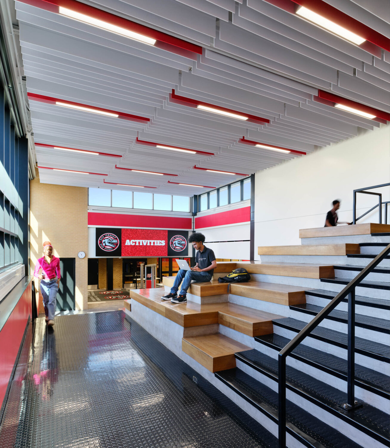 Bleacher steps rising beside a red stair in a commons with a slatted ceiling at Rich Township High School