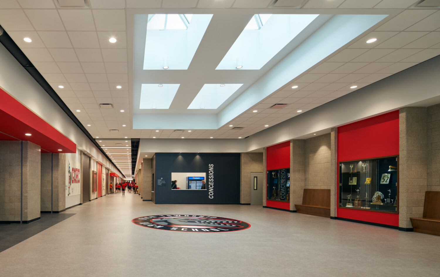 Wide terrazzo corridor with skylights, red accent walls and the school seal on the floor at Rich Township High School