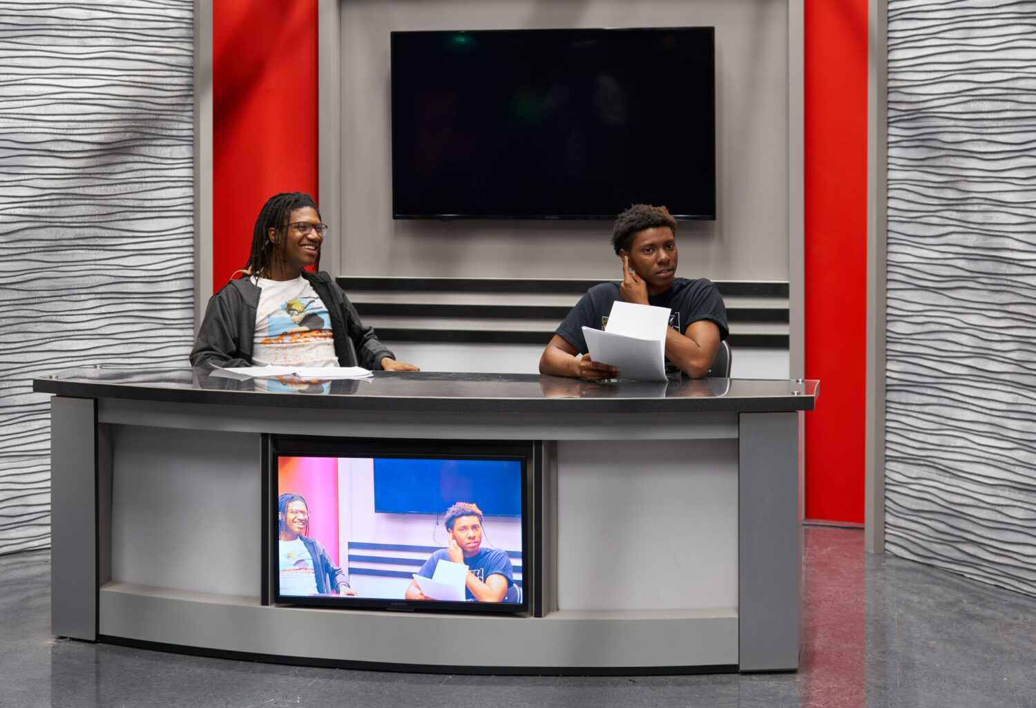 Two students reading the news at a curved anchor desk in the broadcast studio at Rich Township High School