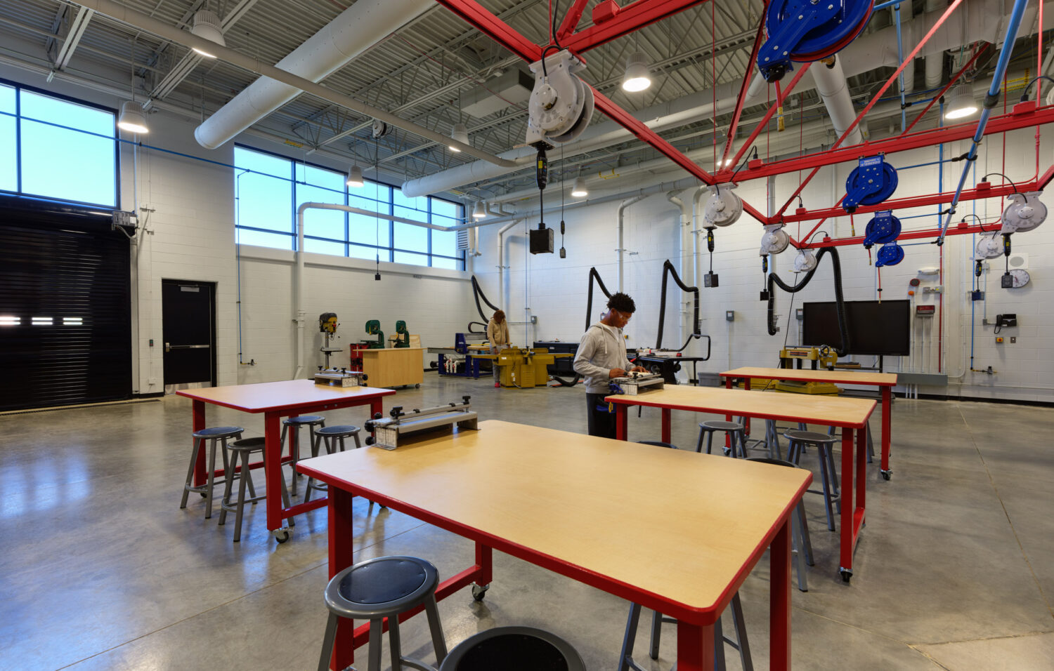 Open lab with wood worktables, red-legged stools and hanging cords from a red ceiling grid at Rich Township High School