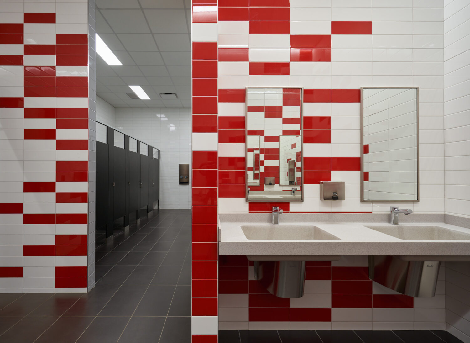 Restroom with red and white glazed tile walls and a long white sink at Rich Township High School