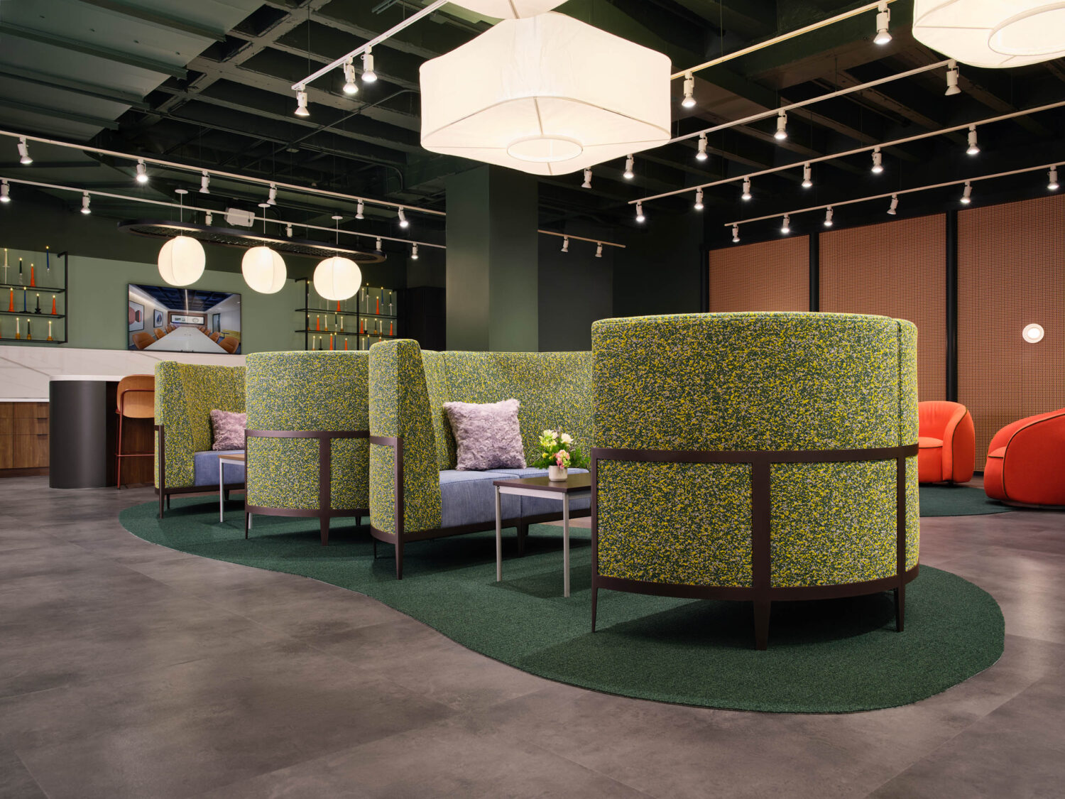 Green upholstered booths on a curving green rug under paper lanterns in the Source International showroom