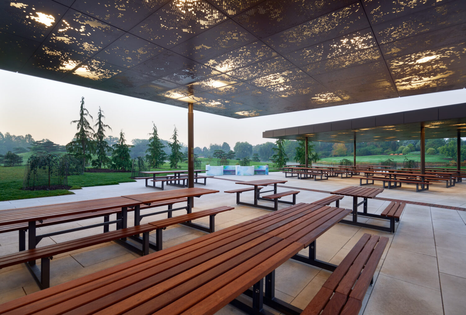 Picnic tables beneath the perforated, backlit canopy of the Chicago Botanic Garden Picnic Glade at dawn