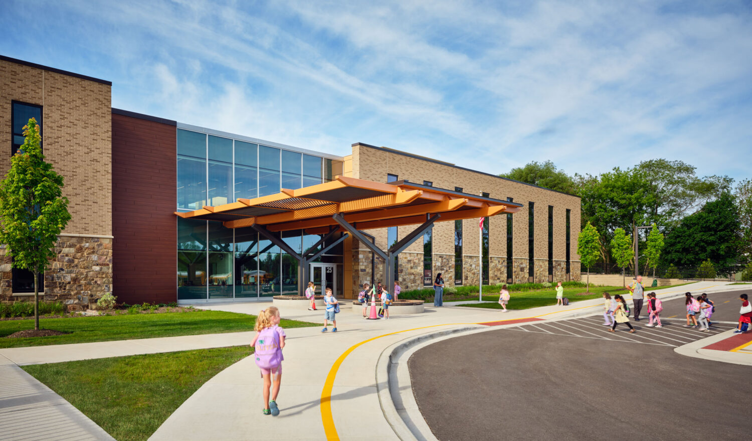 Children walking up the curving entry drive toward the timber and steel canopy of the Kindergarten Center at Churchill Elementary