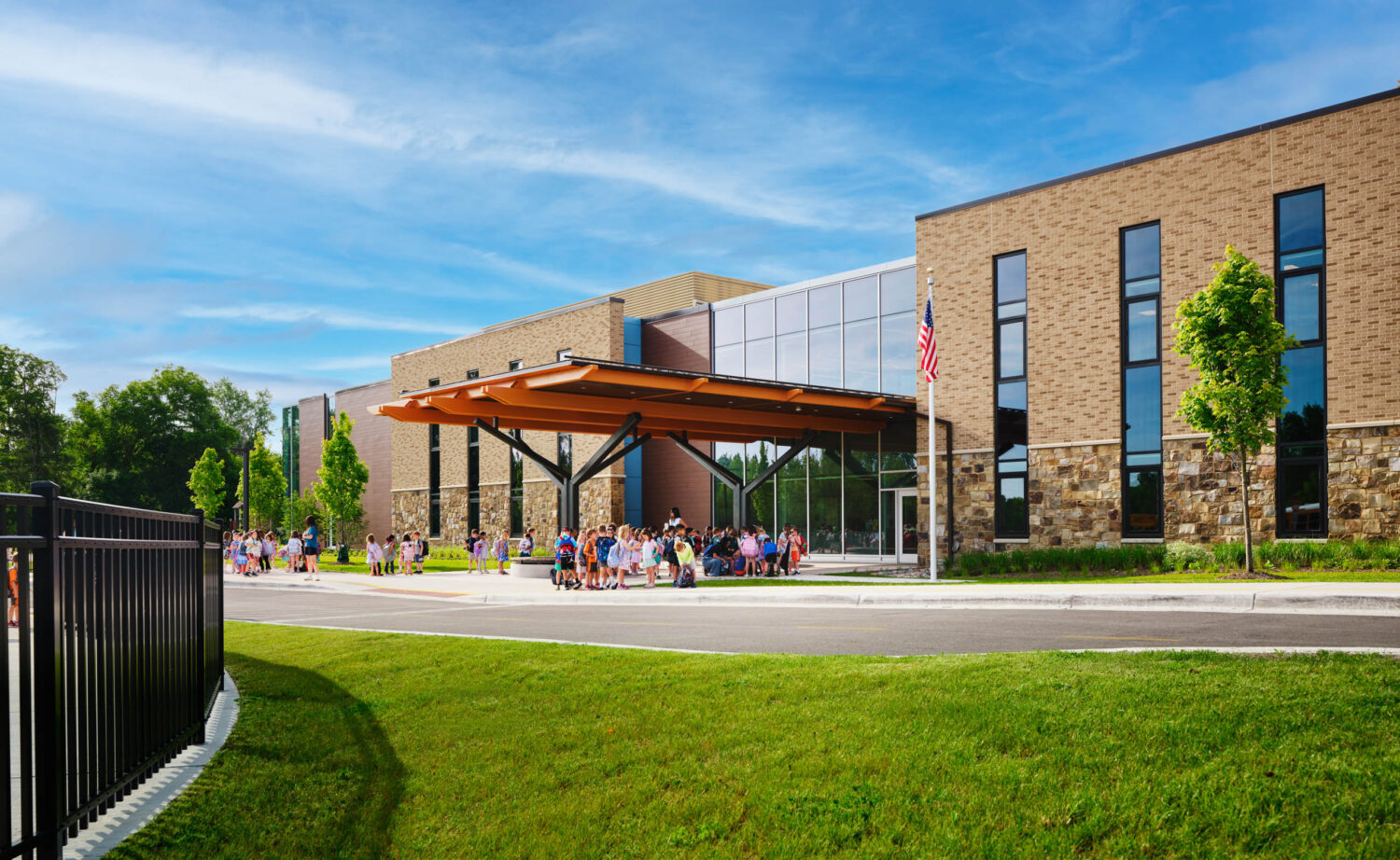 Brick facade and arrival canopy of the Kindergarten Center at Churchill Elementary across a green lawn, with families gathered at the entrance