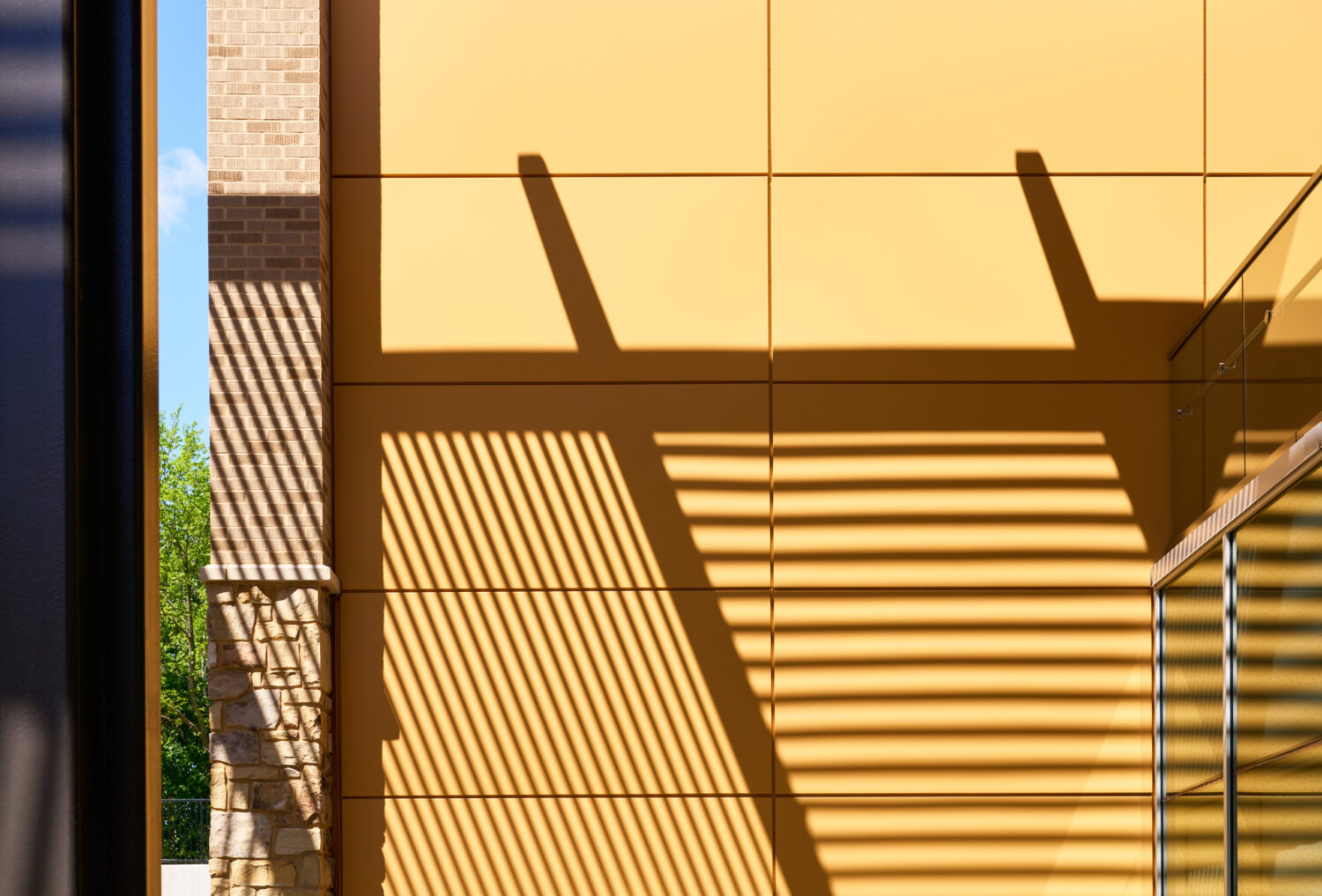 Slatted canopy shadows falling across yellow wall panels and brick at the Kindergarten Center at Churchill Elementary