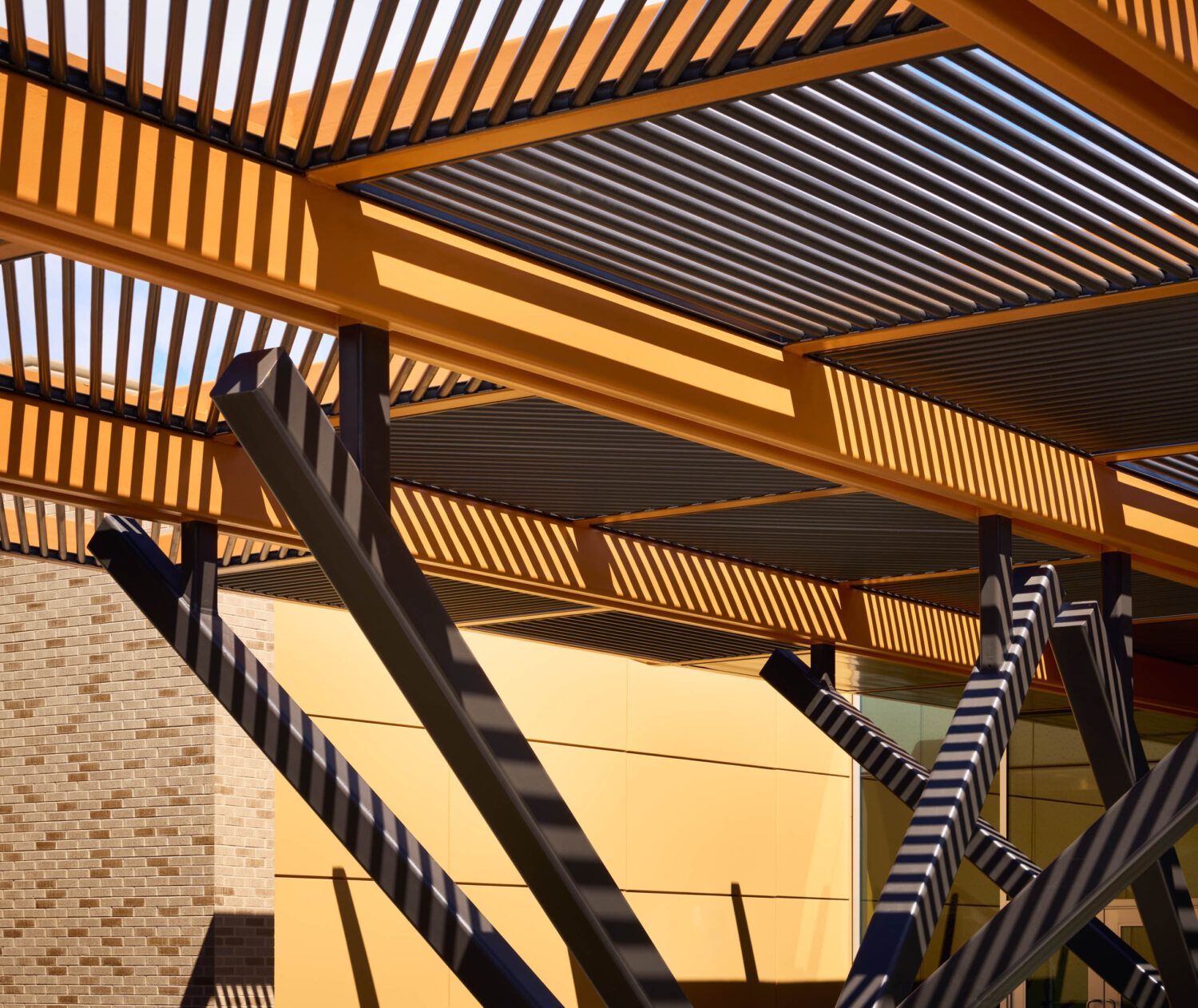 Angled steel columns and timber slats of the entry canopy against yellow panels at the Kindergarten Center at Churchill Elementary