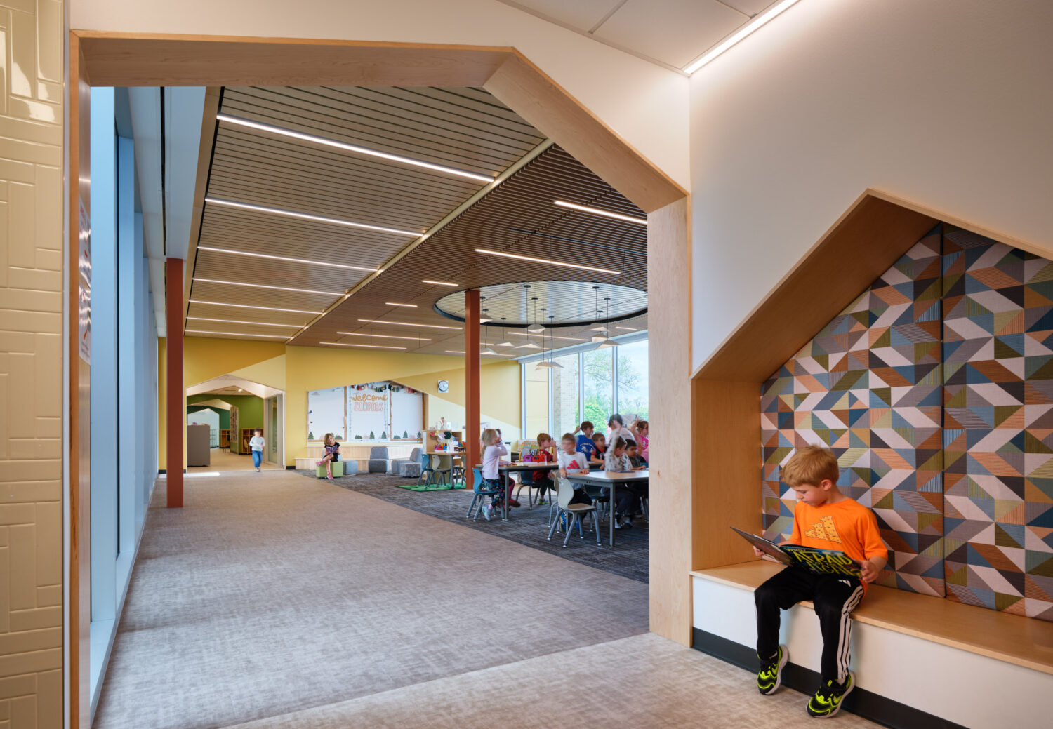 Boy reading in a house-shaped wall nook along a corridor that opens to the learning commons at the Kindergarten Center at Churchill Elementary