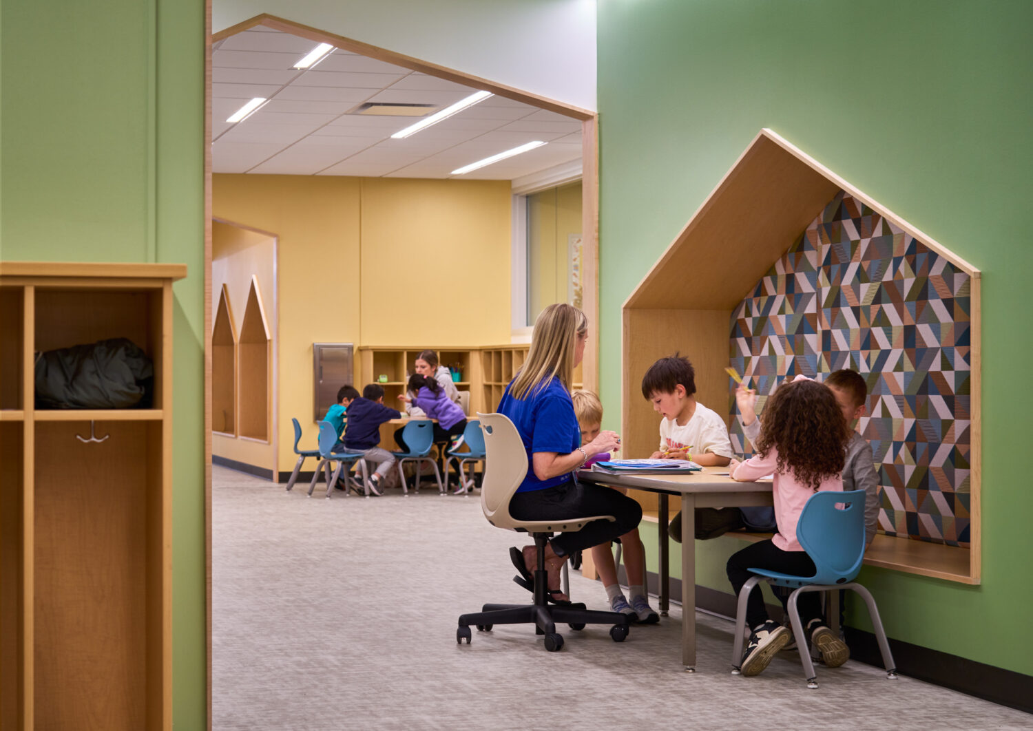 Teacher working with children at a table beside a house-shaped reading nook in a classroom at the Kindergarten Center at Churchill Elementary