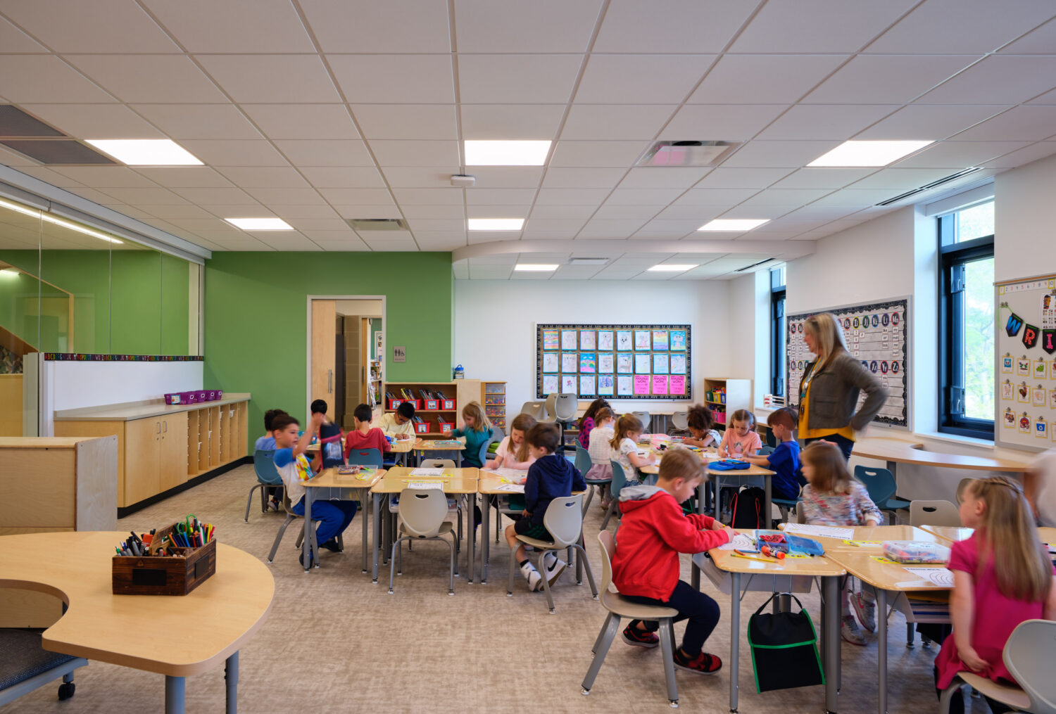 Teacher and children at tables in a green-accented kindergarten classroom at the Kindergarten Center at Churchill Elementary